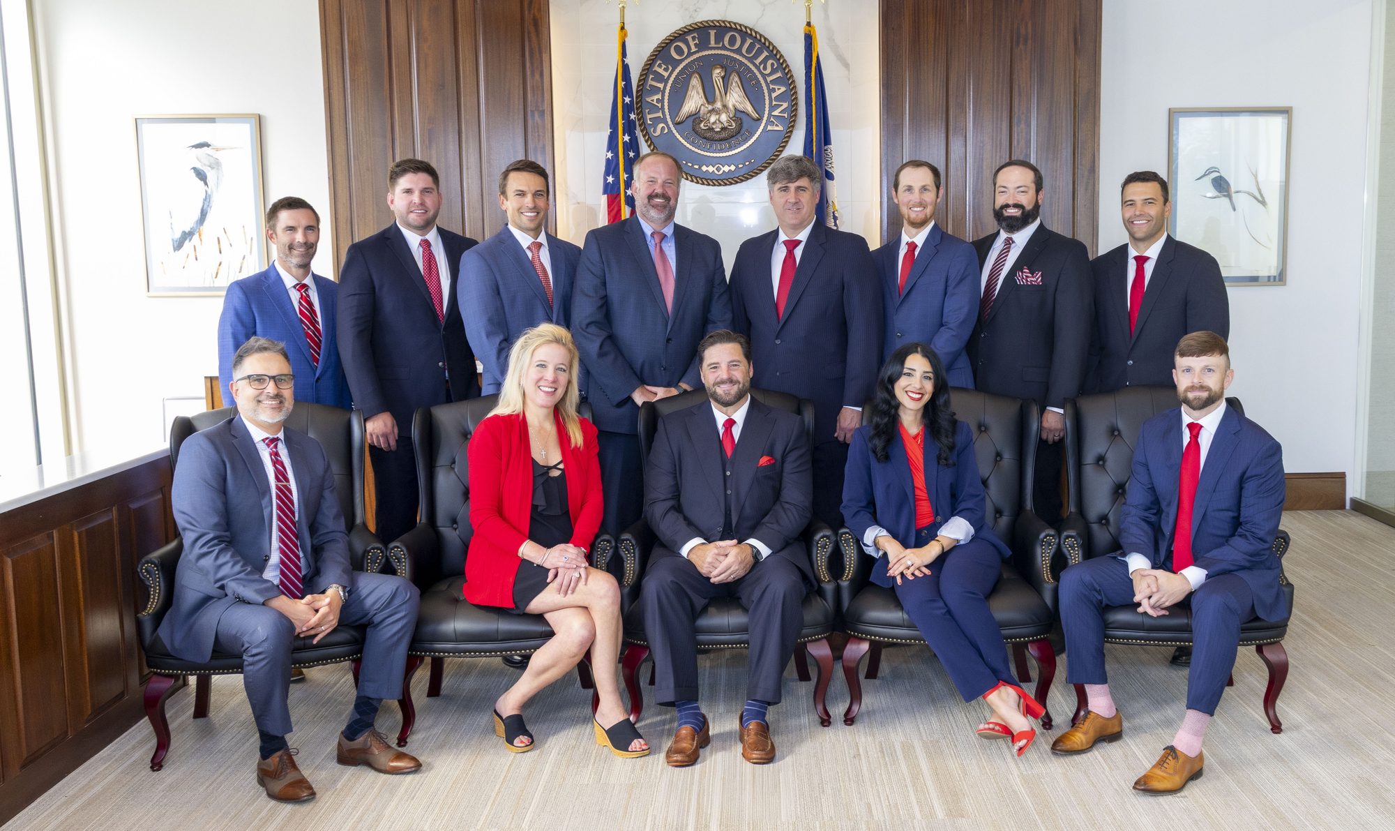 The thirteen people of Spencer Calahan Injury Lawyers, eight standing behind five seated in leather chairs, in the firm's wood-panelled conference room under the Louisiana state seal.